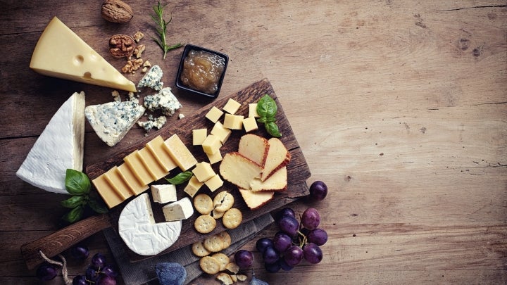 Fettarmer Käse: Ansprechende Käseplatte, verschiedene Käsesorten auf Holzbrett, verziert mit Trauben und Feigen.