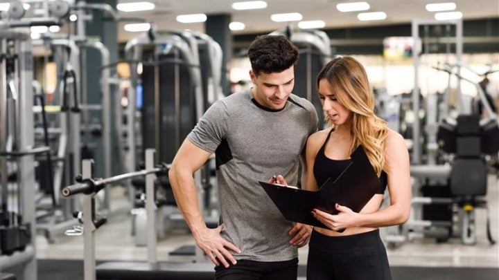 Frau im Fitnessstudio zeigt Mann Trainingsplan.